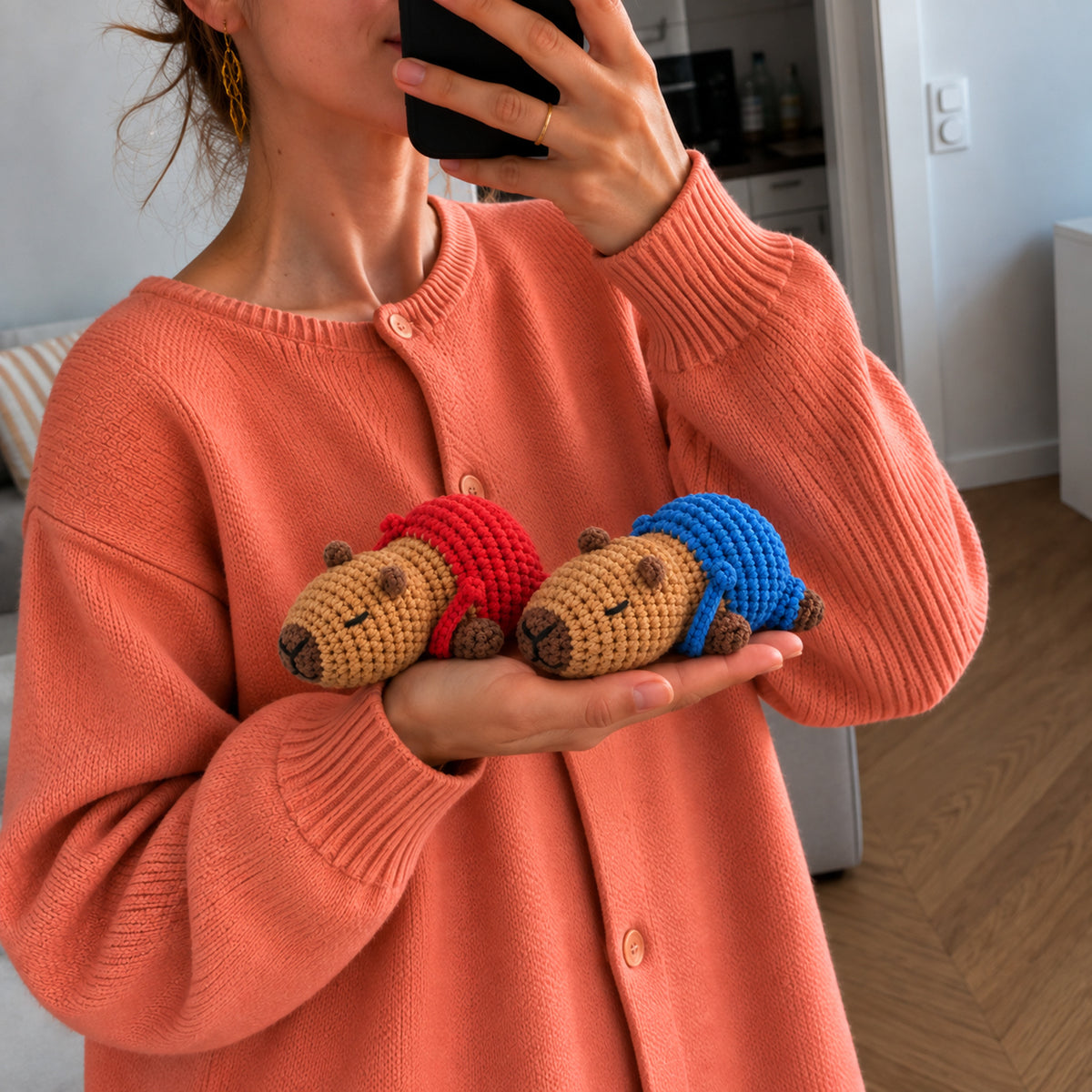 Cozy Coat Capybaras: resting capybaras in bright red and blue coats, shown in hand